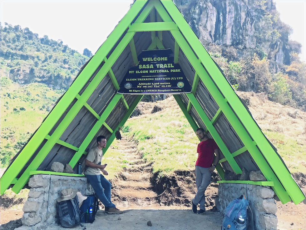 Sasa Trail entrance sign, two people, Mount Elgon National Park welcome sign, hiking trail.