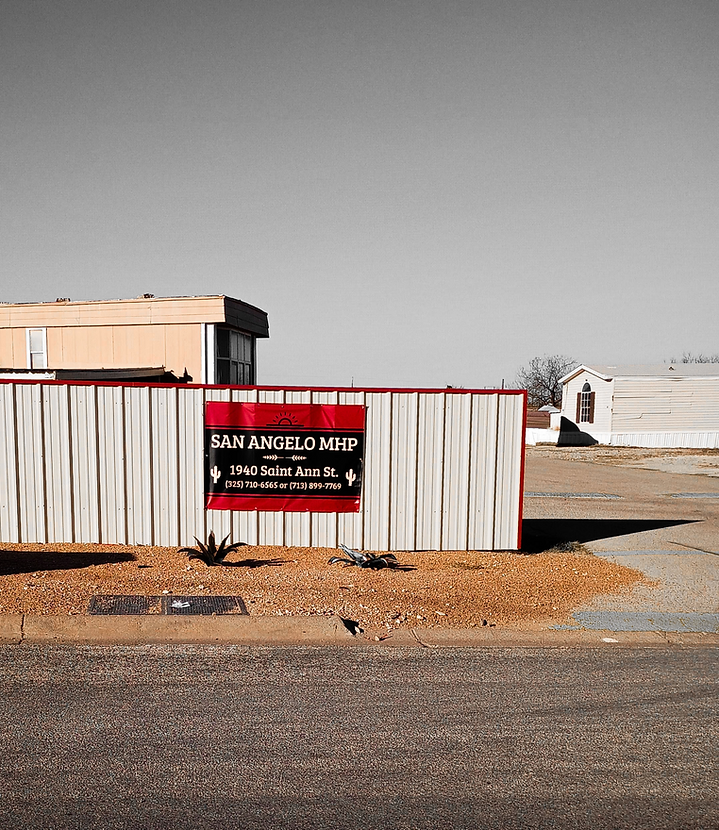 San Angelo Mobile Home Park entrance sign on a metal fence with mobile homes and sky in the background