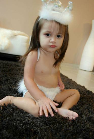 Curious toddler with a white fur crown sitting on a rug. In-Home photo shoot at Miami , Emerald Estates