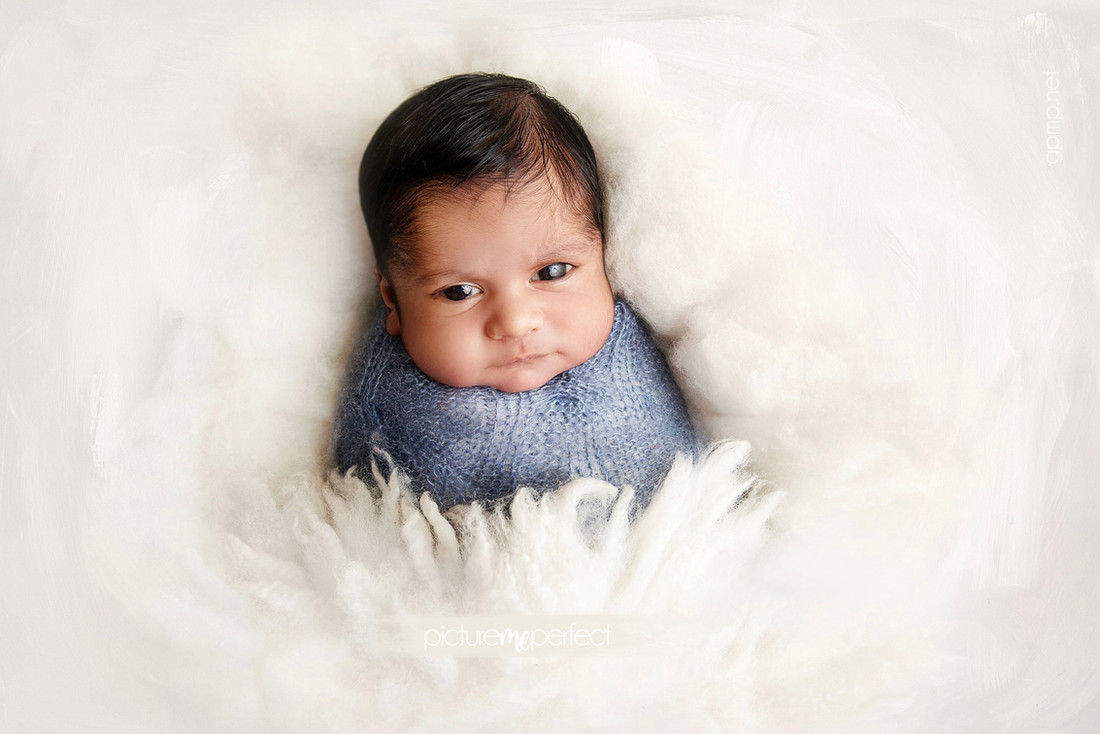 Awake newborn in a blue swaddle on white fluff. At his home in Miami Lakes Main Street area