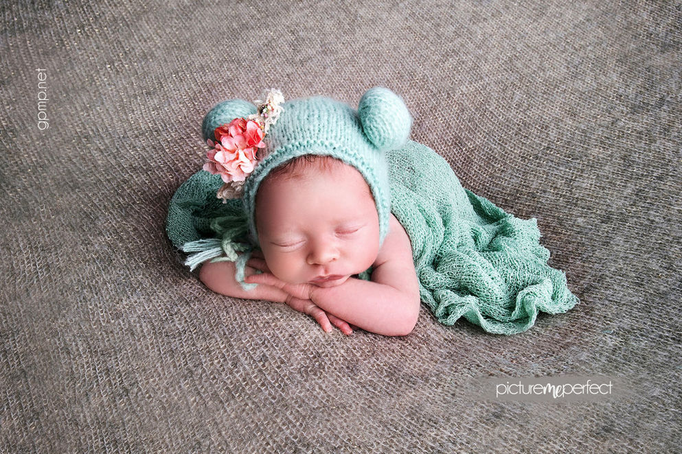Newborn baby girl sleeping in a mint knitted with ears bonnet with pink flowers. Posing tummy down. Canarias at Downtown Doral