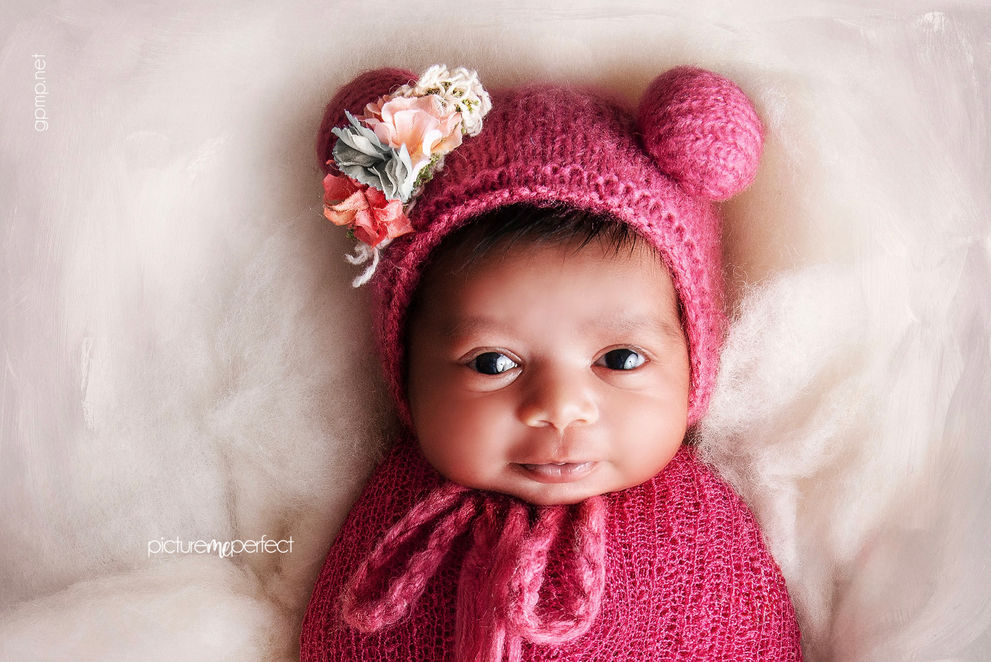 Smiling 5 days old newborn baby girl in fucia knitted bonnet with flower. Miami Savanna photo shoot
