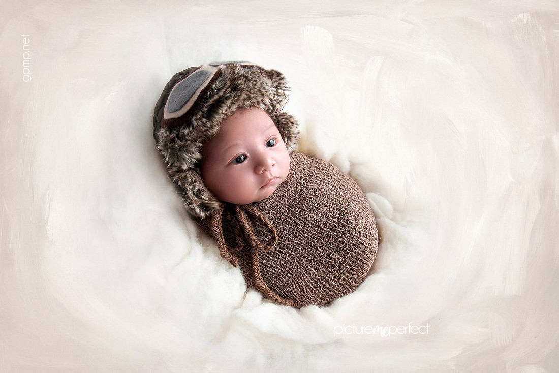 Awake newborn in pilot hat and brown wrap, At his home in Miami Lakes Main Street area