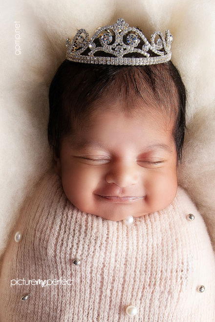 Smiling newborn baby girl in a pearl-studded pink swaddle and crown. Miami photo session at The Ridges