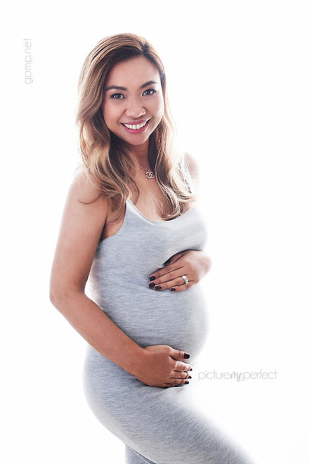 Smiling pregnant woman cradling her belly, light grey dress, sweetwater
