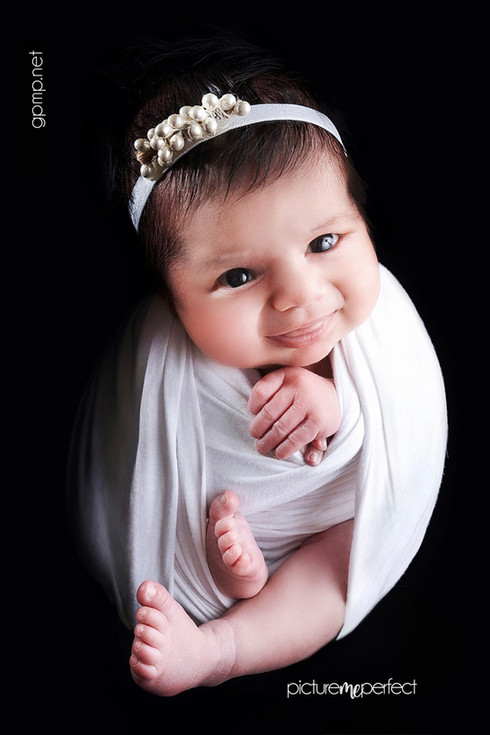 Smiling newborn baby wrapped in white with a pearl headband, on at Miami, Miami Lakes,Royal Oaks