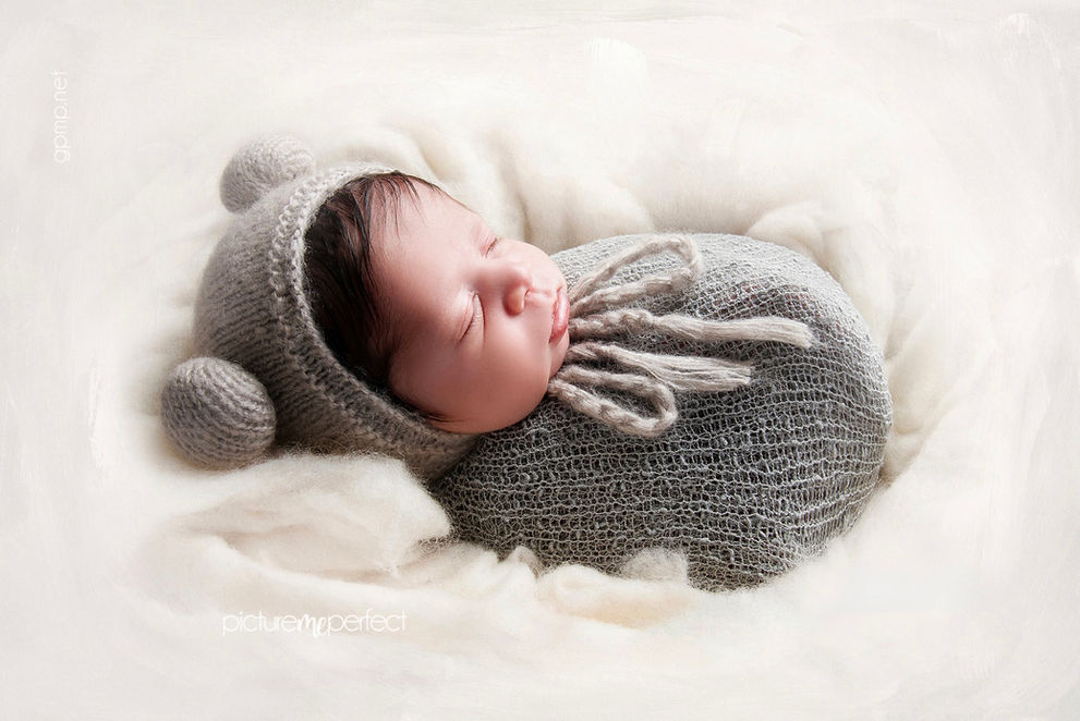 Newborn baby sleeping peacefully in gray knitted bear bonnet and swaddle. Canarias at Downtown Doral