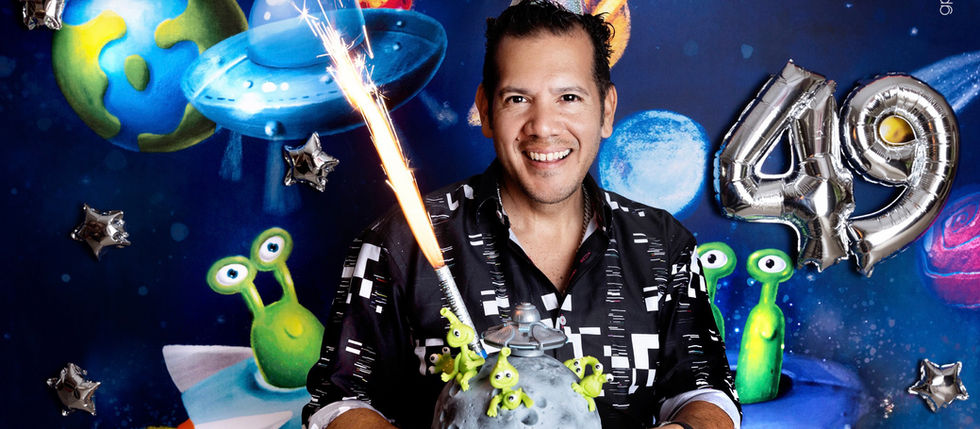 Man celebrating his 49th birthday with an alien-themed cake, space decorations, and alien party backdrop