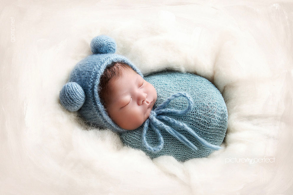 Newborn baby boy sleeping in blue knitted wrap and bonnet, posing in white wool. Canarias at Downtown Doral