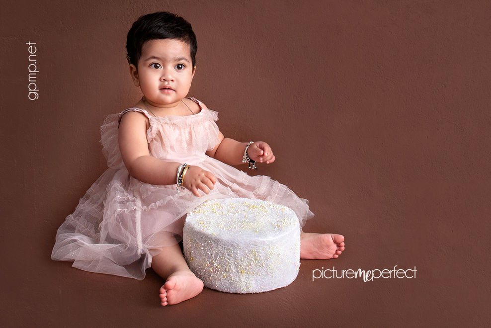 Baby in pink dress next to a white cake Coral Gables