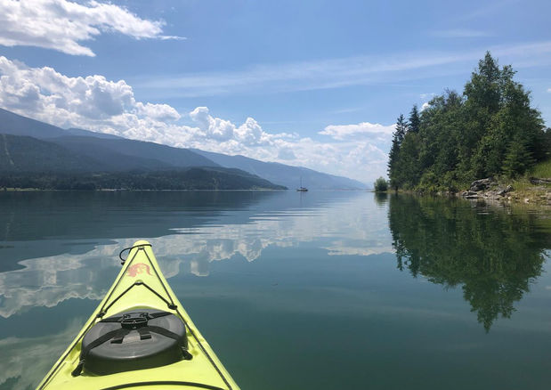 Kayaking on calm Arrow Lake with mountain reflections near Hummingbird Cabins 'n' Breakfast in British Columbia