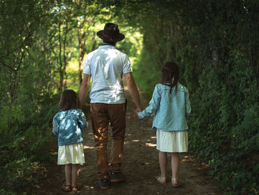 Benjamin marchant main dans la main avec ses deux filles dans un chemin forestier