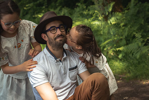 Un père entouré de ses deux filles qui l'embrassent avec tendresse lors d'une séance photo famille en extérieur