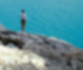Woman standing on the edge of a mountain overlooking the ocean on a sunny day, symbolizing control, balance, and sexual wellness practices like edging vs. gooning.