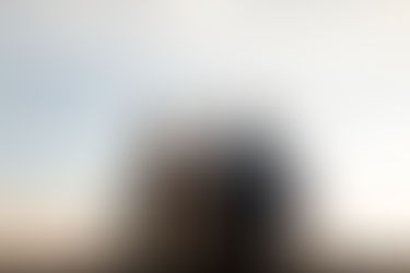 Elderly couple sitting on a ledge, embracing and gazing into each other's eyes during sunset. Calm, warm ambiance with cloudy sky.