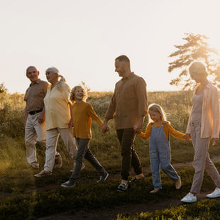 Family of six walking hand in hand in a sunlit field, wearing casual clothes. The scene is serene, with warm sunlight and an open sky.