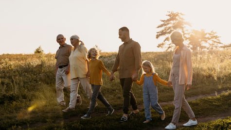 Family of six walking hand in hand in a sunlit field, wearing casual clothes. The scene is serene, with warm sunlight and an open sky.