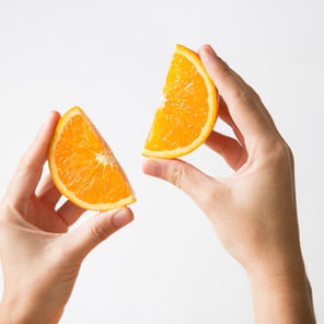 Hands hold two vibrant orange slices against a plain white background, suggesting freshness and simplicity.