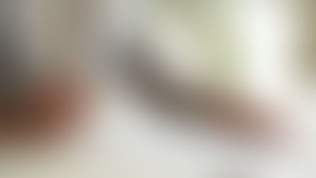 Person in a light gray suit writing on a document at a desk with a pen in hand. Bright office setting with blurred shelves and plant.