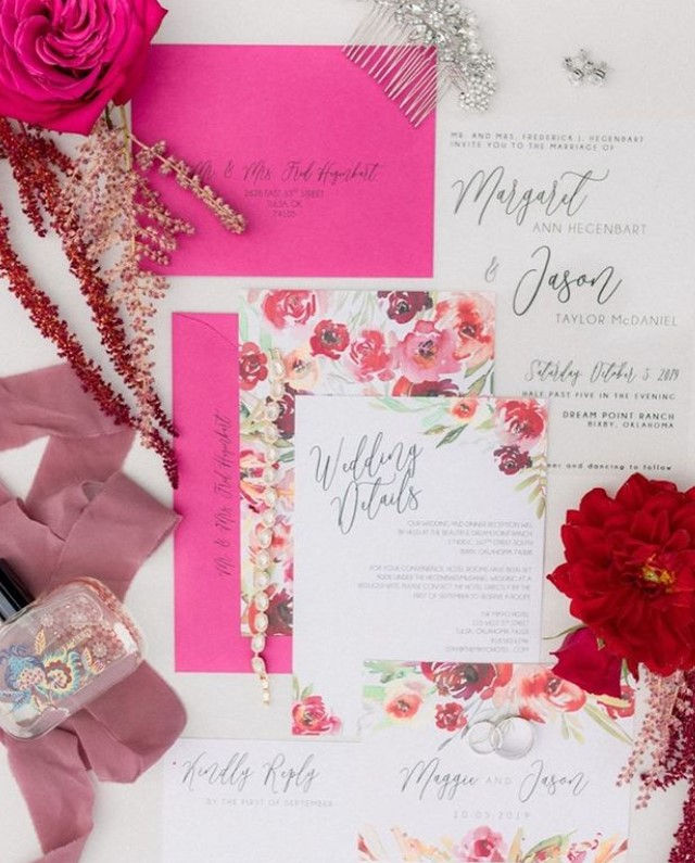 A details shot of invitations and wedding cards with floral designs and pink and red colors.