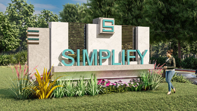  Daytime view of a custom monument sign featuring teal “SIMPLIFY” letters, stone base, decorative panels, and surrounding greenery.