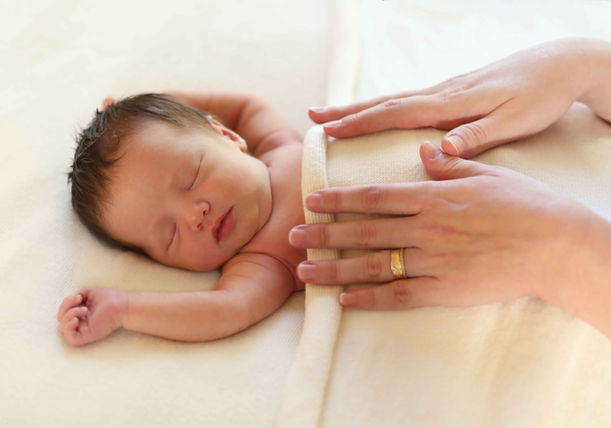 A peaceful sleeping newborn baby with a mother's gentle hands resting tenderly on them during an in-home photography session in Atlanta.