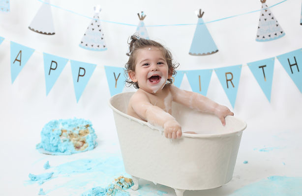 Baby smiling beside first birthday cake during cake smash photography session