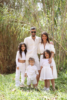 A smiling family of five wearing stylish all-white outfits standing together in a lush outdoor setting surrounded by tall bamboo stalks during a family photo session in Atlanta.