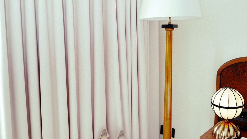 A pair of high heels and papers sit on a small round table with gold legs. Nearby, a floor lamp and a nightstand with a globe lamp.