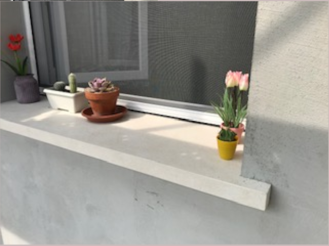 Davanzale esterno in pietra chiara con piccole piante grasse in vasi di terracotta e fiori colorati, situato davanti a una finestra con zanzariera.