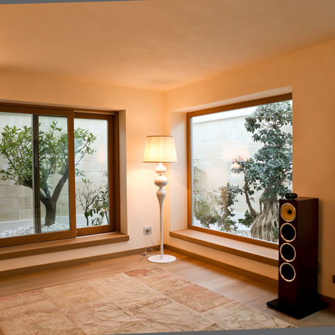 Interno di un soggiorno moderno con ampie finestre e una porta scorrevole in legno naturale che si affacciano su un patio interno con piante