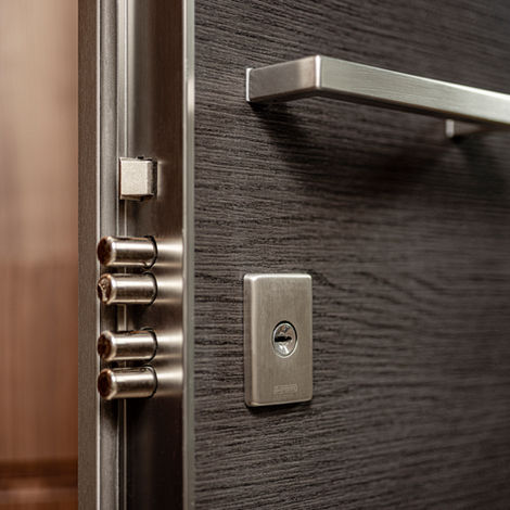 Primo piano dei catenacci in acciaio di una serratura blindata a ingranaggi su porta in legno scuro, con maniglia e cilindro europeo in finitura satinata.