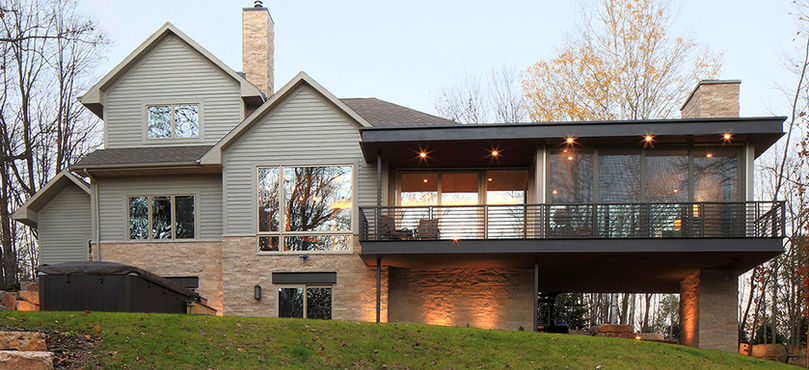 Exterior of new four season addition (on right) with wrap-around deck, tinted windows, and brick fireplace.