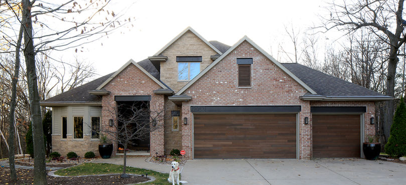 Curb-side exterior features brick peaks, steel beams, and custom-made garage doors.