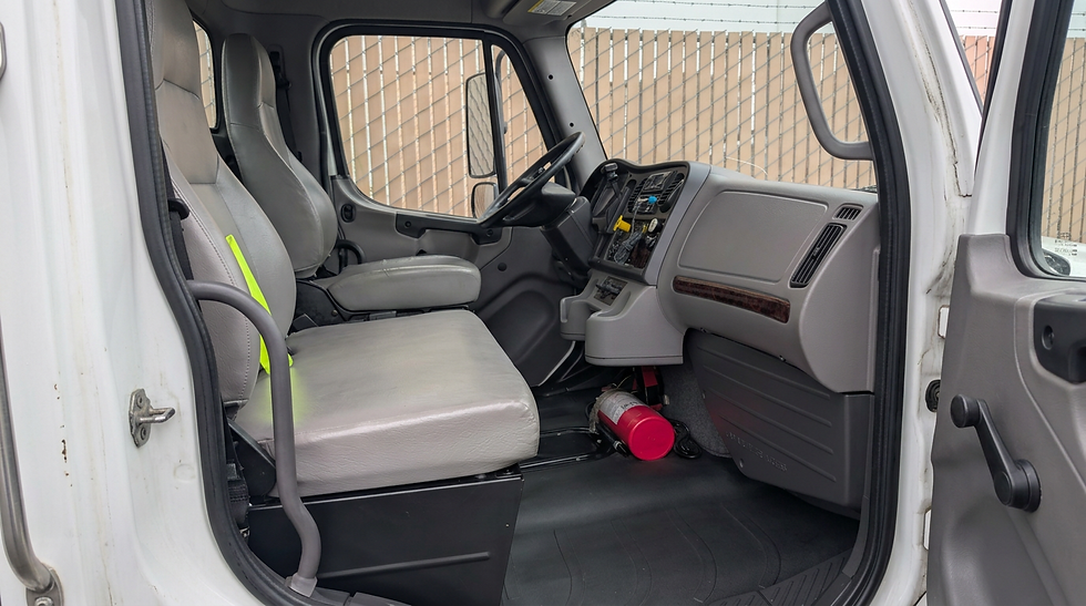 Studio photography of the interior cab of a commercial truck. The shot highlights the clean dashboard, driver and passenger seating, and a fire extinguisher, conveying a professional and functional environment.