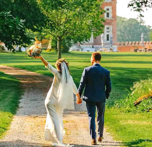 Mariés main dans la main dans l’allée d’un château du Nord, la mariée levant son bouquet