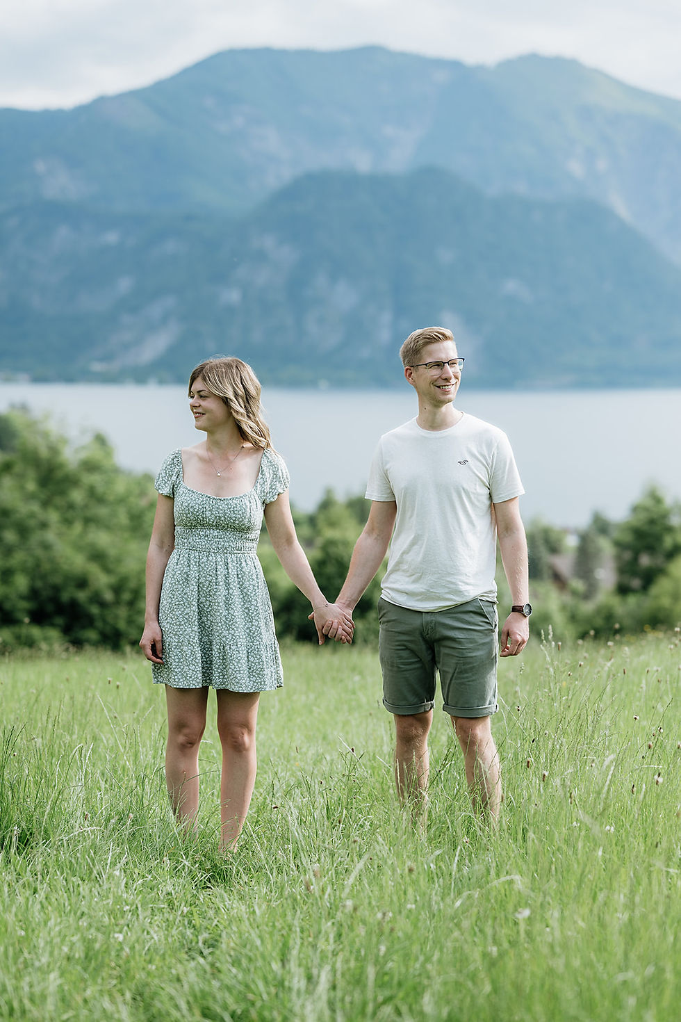 Coupleshooting am Attersee – Verlobungspaar steht auf einer Wiese mit Blick auf den See im Salzkammergut.
