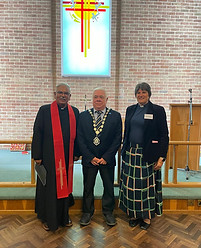 Witham Mayor in a suit and his chains of office, stood in a church between two members of the church, one of whom is the reverend in his robes