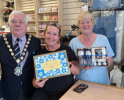 Witham Mayor Councillor Paul Heath in a suit and his chains with two ladies from haberdashery Rag, Tag & Bobtail, one holding a framed certificate and one a prize hamper that they have been awarded for winning the Dementia Awareness Week window competition