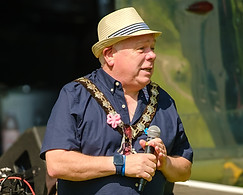 Witham Town Mayor, Councillor Paul Heath at our United in Music Festival. Paul is holding a microphone and wearing his chain, a blue short sleeved shirt and a straw boater hat