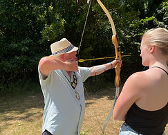 Witham Mayor Cllr Paul Heath with an archery bow & arrow taking aim while watched by a lady who we can only see from the back.