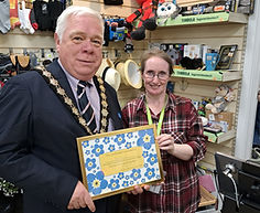 Witham Mayor Councillor Paul heath presenting a framed certificate to a lady from Barnardos charity shop for participating in the Dementia Awareness Week window competition