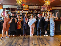 Witham Mayor Cllr Paul Heath, wearing a suit and Mayoral chains, along with the Deputy Mayor also in a suit, with a mixed group of 6 people. The lady in the middle wearing a pink trouser outfit, is holding an oversized cheque