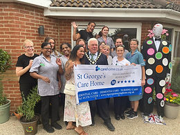 Witham Mayor Cllr Paul Heath in his chains with a group of staff outside the nursing home holding up banner showing their achievements