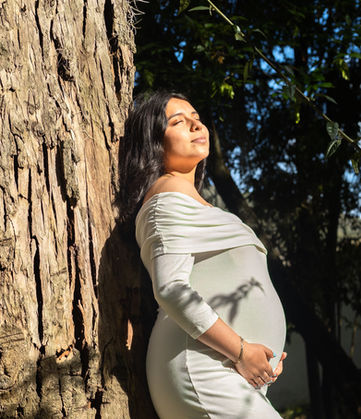 Mujer embarazada apoyada en un árbol, manos en el vientre