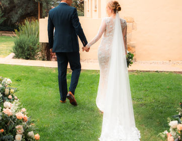 Novios caminan de la mano en jardín tras boda