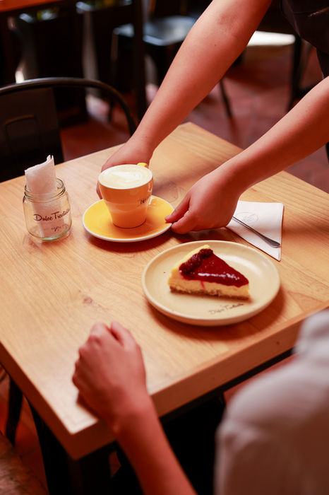 Manos colocando café y pastel en una mesa.