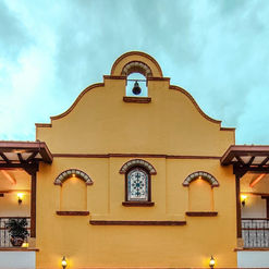 Fachada de edificio amarillo con campana y balcones