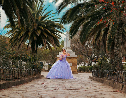 Quinceañera en vestido lavanda en jardín con palmeras.