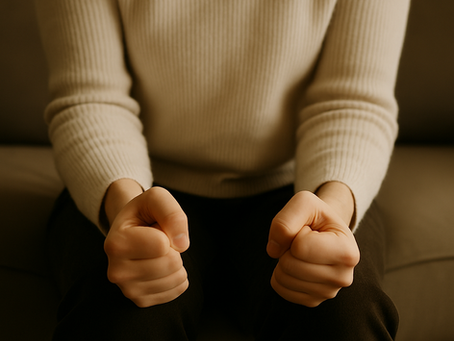 Eine Person sitzt auf einem Sofa, die Hände zu Fäusten geballt. Der Fokus liegt auf den angespannten Händen und Unterarmen. Die warme Lichtstimmung und das neutrale Setting spiegeln zurückgehaltene Wut und innere Spannung wider – ohne laut zu sein.